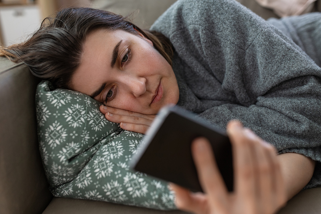 Eine Frau liegt auf der Couch und scrollt auf ihrem Handy durch soziale Medien.