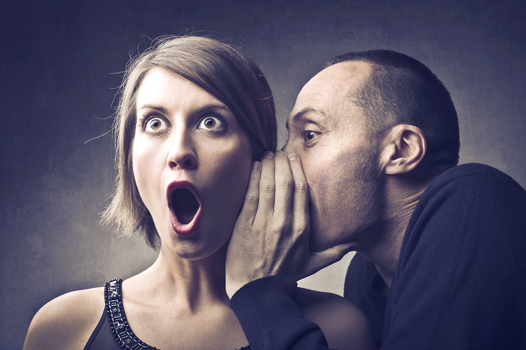 Ein Mann flüstert einer Frau ein schockierendes Geheimnis ins Ohr. Sepia-Effekt.